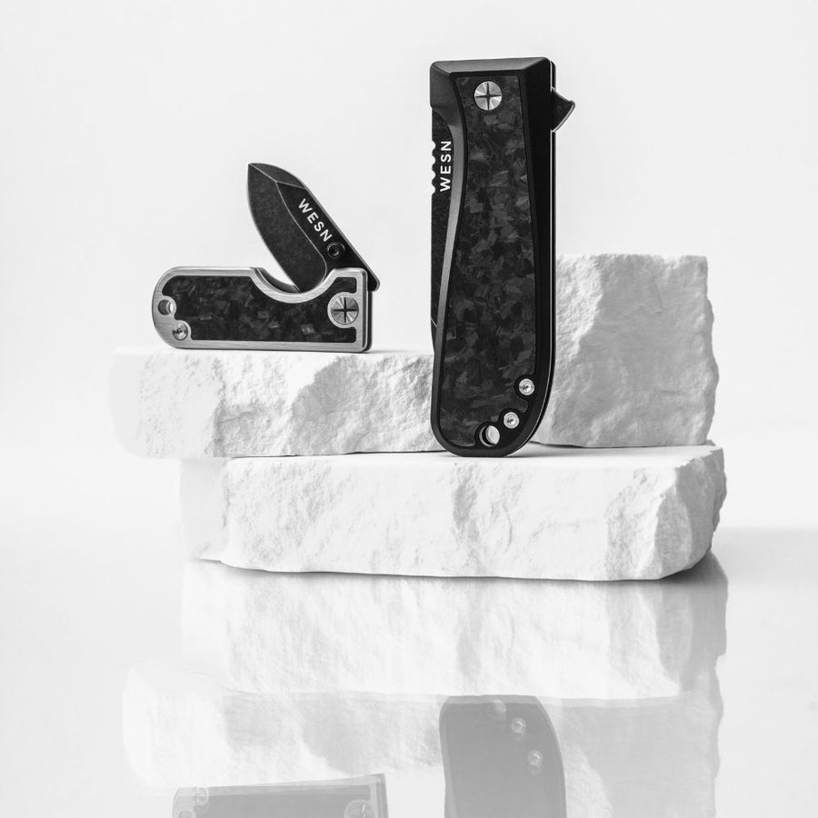 Two folding knives on a white marble block with 'WESN' branding.